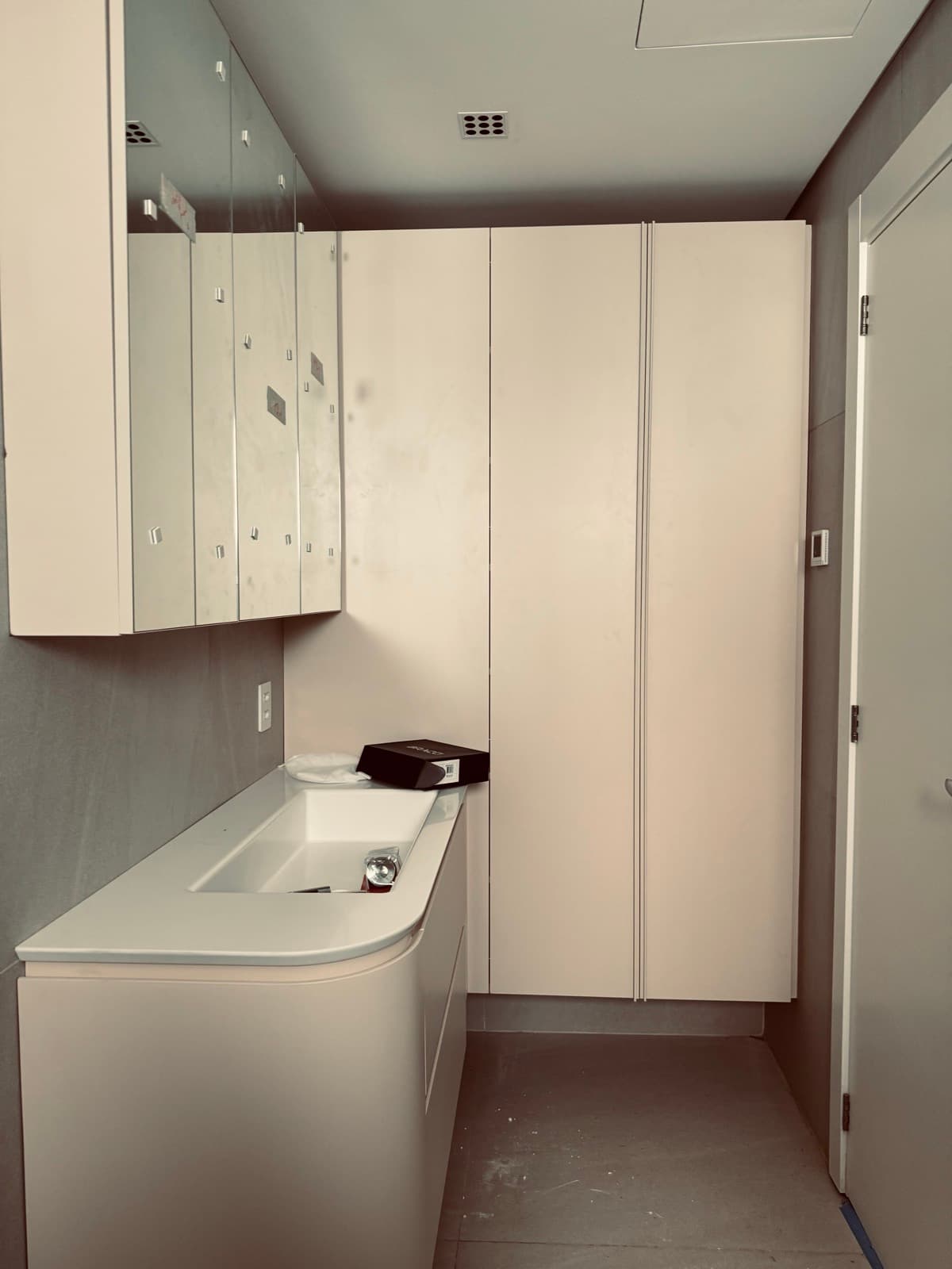 A bathroom being fitted out, with pale cabinets and a curved vanity still to be cleaned